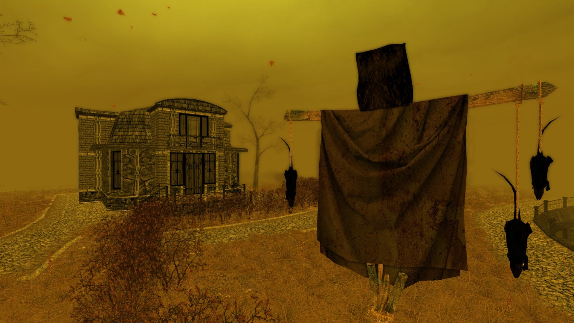 A screenshot from Pathologic showing a yellow landscape - yellow sky, yellow grass - with a squat stone home in the background and a makeshift scarecrow in the foreground, dead rats hanging from its arms